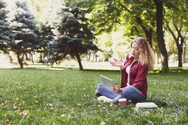 Young casual woman with tablet and notebooks outdoors. Female student preparing for exams with books and coffee in the park. Education and entering the university concept, copy space.