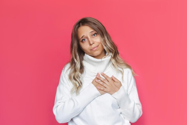 Photo young caucasian attractive blonde woman with wavy hair in white sweater holds her hands on chest