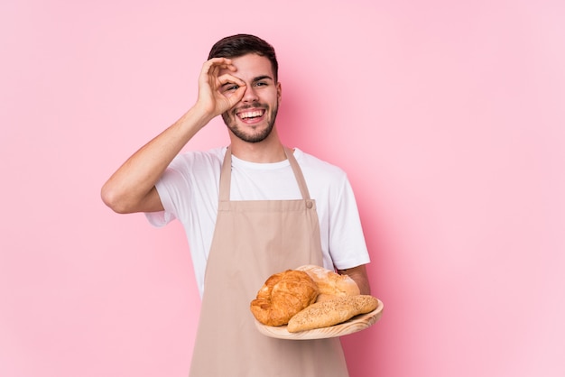 Il giovane uomo caucasico del panettiere ha isolato eccitato mantenendo il gesto giusto sull'occhio.