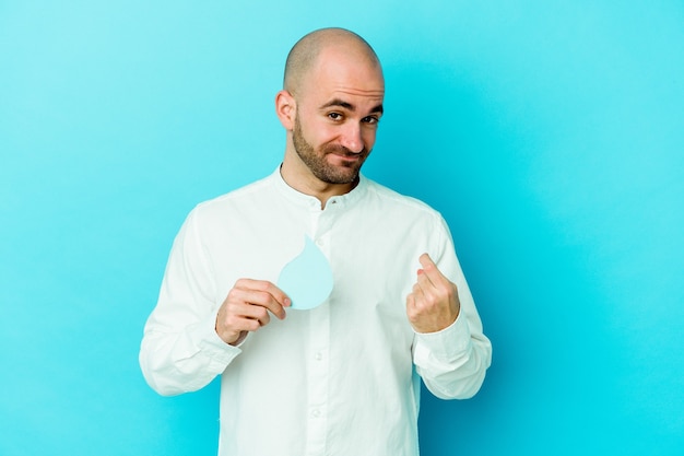 Young caucasian bald man celebrating world water day isolated on blue pointing with finger at you as if inviting come closer.