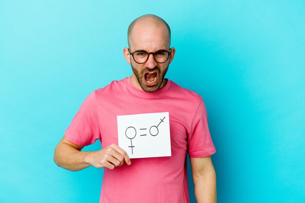 Young caucasian bald man holding a equality gender placard isolated on yellow wall screaming very angry and aggressive