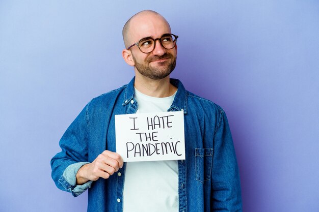 Young caucasian bald man holding a I hate the pandemic placard isolated on blue background dreaming of achieving goals and purposes