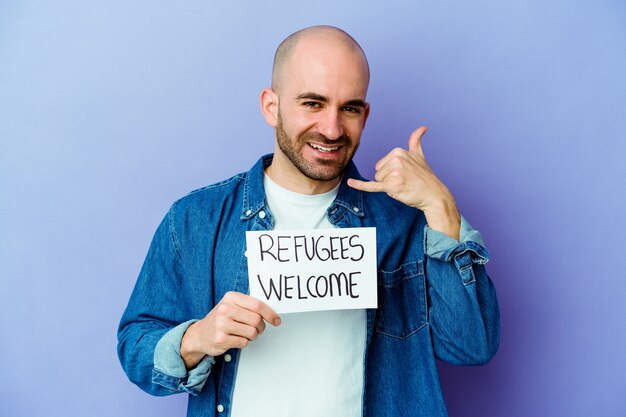 Young caucasian bald man holding a Refugees welcome placard isolated on blue background showing a mobile phone call gesture with fingers.