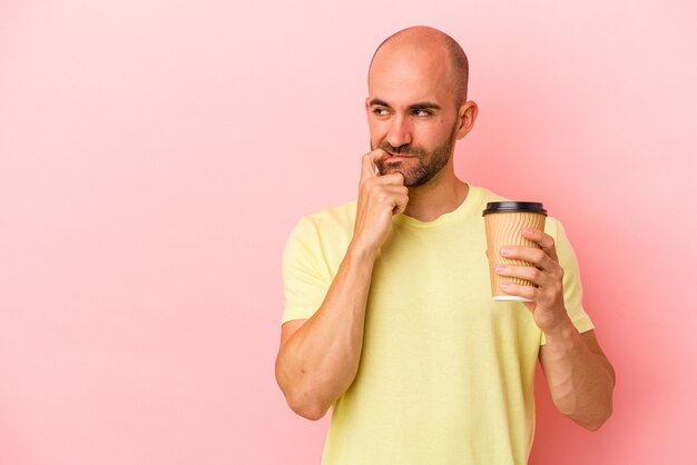 Young caucasian bald man holding a take away coffee isolated on pink background  relaxed thinking about something looking at a copy space.