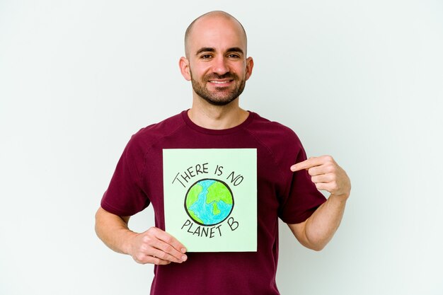 Young caucasian bald man holding a there is not planet B placard isolated on purple background person pointing by hand to a shirt copy space, proud and confident