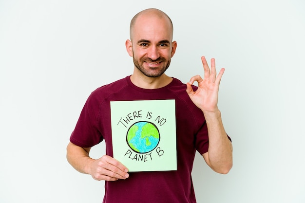 Young caucasian bald man holding a there is not planet B placard isolated on purple wall cheerful and confident showing ok gesture.