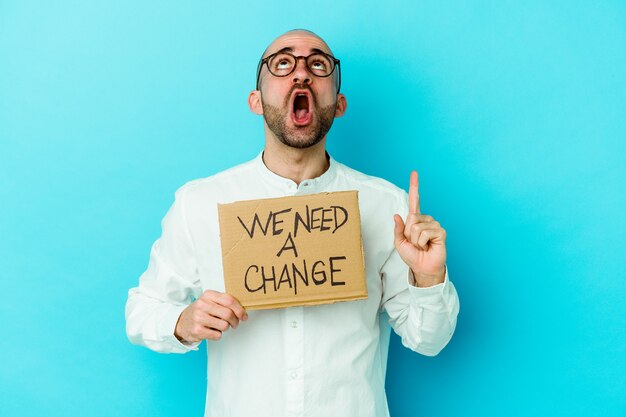 Young caucasian bald man holding a We need a change placard isolated on purple wall pointing upside with opened mouth.