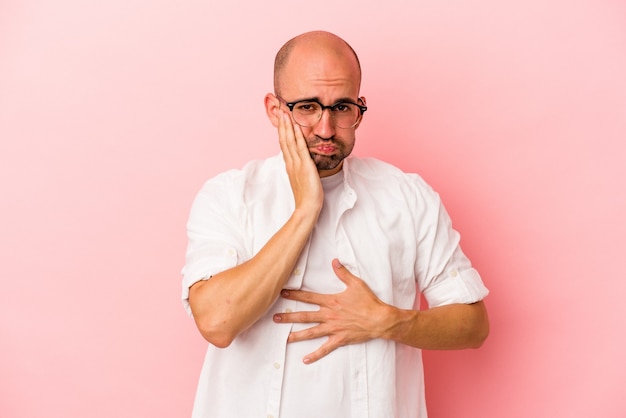 Young caucasian bald man isolated on pink background  blows cheeks, has tired expression. Facial expression concept.