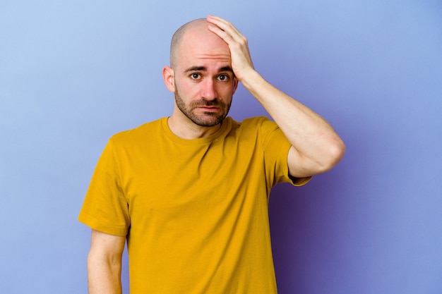 Young caucasian bald man isolated on purple background being shocked, she has remembered important meeting.