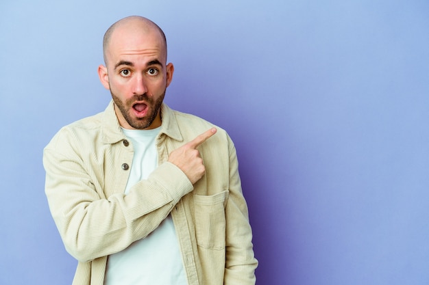 Young caucasian bald man isolated on purple background pointing to the side