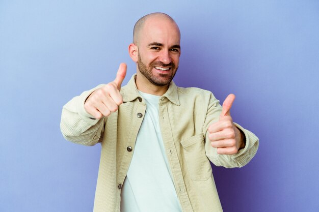 Young caucasian bald man isolated on purple background raising both thumbs up, smiling and confident.