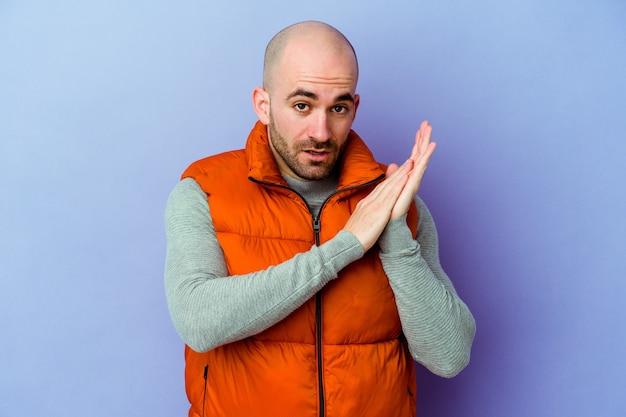 Young caucasian bald man isolated on purple wall feeling energetic and comfortable, rubbing hands confident