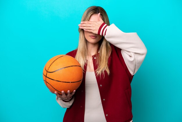 Young caucasian basketball player woman isolated on blue background covering eyes by hands Do not want to see something