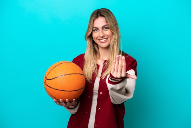 Young caucasian basketball player woman isolated on blue background inviting to come with hand Happy that you came