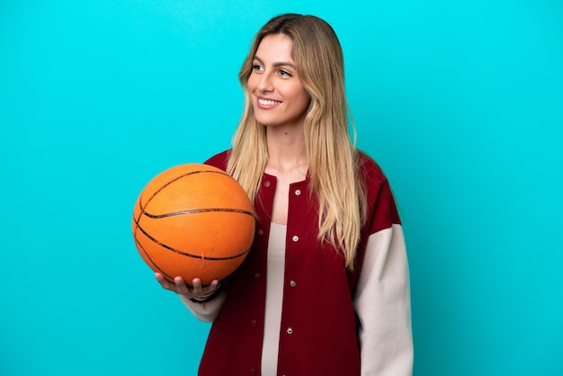 Young caucasian basketball player woman isolated on blue background looking side