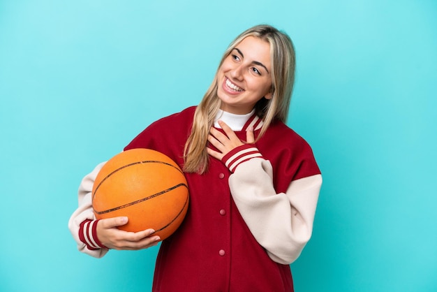 Young caucasian basketball player woman isolated on blue background looking up while smiling