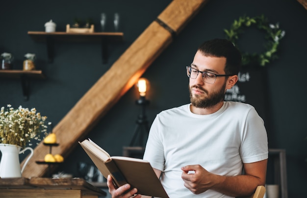 Young caucasian bearded man reading a book in the kitchen. Home leisure.