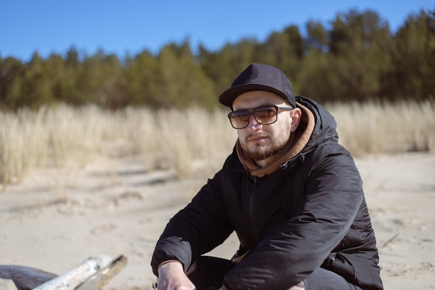 Young caucasian bearded man sits on a log on sandy beach