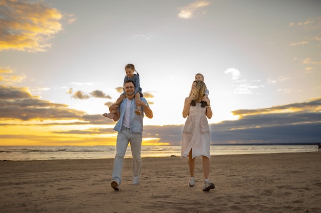 young caucasian beautiful couple with kids on theirr shoulders on sunset at the beach in summer