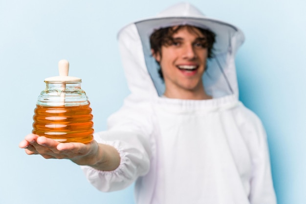青い背景に分離された蜂蜜を保持している若い白人の養蜂家の男