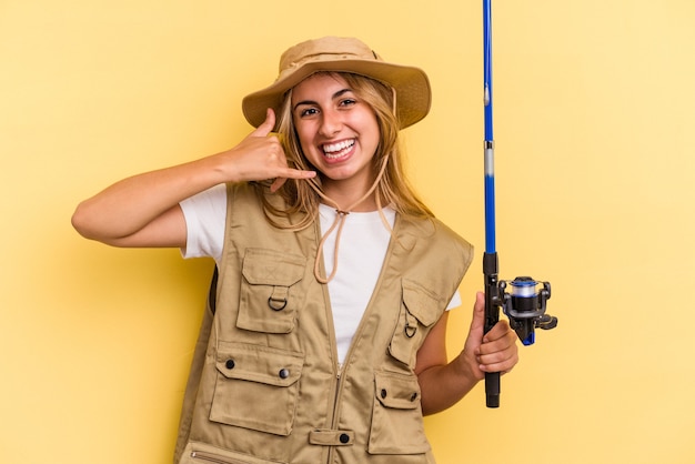 Young caucasian blonde fisherwoman holding a rod isolated on yellow background  showing a mobile phone call gesture with fingers.