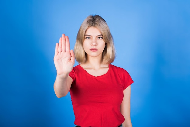 Young caucasian blonde girl in casual clothes showing stop\
gesture with hand and palm reject sign isolated on studio blue\
background