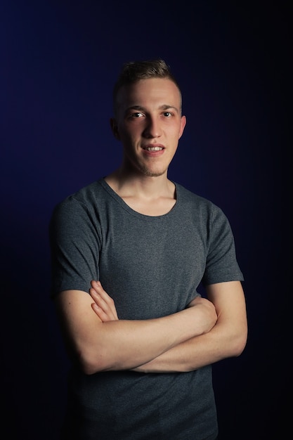 Young caucasian blonde man in grey t shirt on dark purple background.