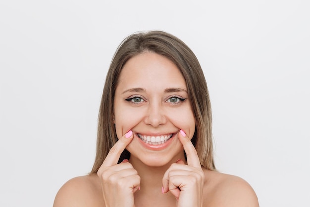 young caucasian blonde woman demonstrating her beautiful smile with fingers on a white background