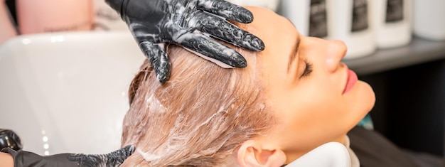 Giovane donna bionda caucasica con i capelli lavati nel lavandino in un salone di bellezza.