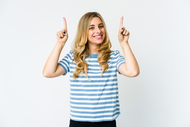 Young caucasian blonde woman indicates with both fore fingers up showing a blank space.