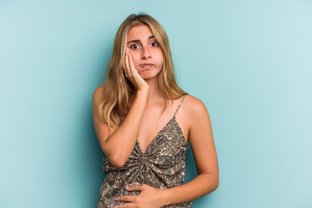 Young caucasian blonde woman isolated on blue background  blows cheeks, has tired expression. Facial expression concept.