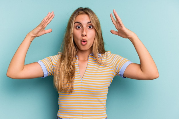 Young caucasian blonde woman isolated on blue background  celebrating a victory or success, he is surprised and shocked.