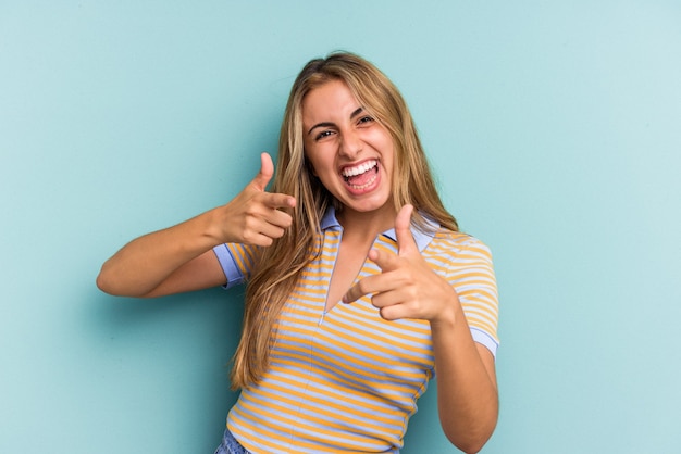 Young caucasian blonde woman isolated on blue background  cheerful smiles pointing to front.