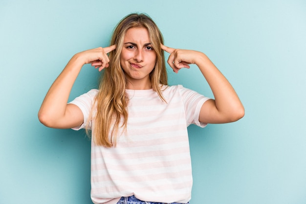 Young caucasian blonde woman isolated on blue background  focused on a task, keeping forefingers pointing head.