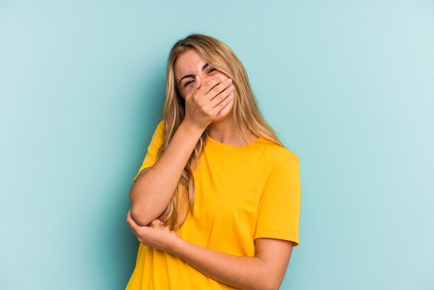 Young caucasian blonde woman isolated on blue background  laughing happy, carefree, natural emotion.