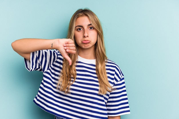 Young caucasian blonde woman isolated on blue background  showing a dislike gesture, thumbs down. Disagreement concept.