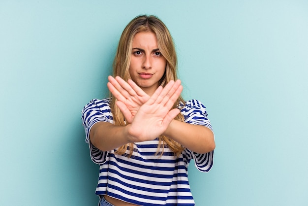 Young caucasian blonde woman isolated on blue background  standing with outstretched hand showing stop sign, preventing you.