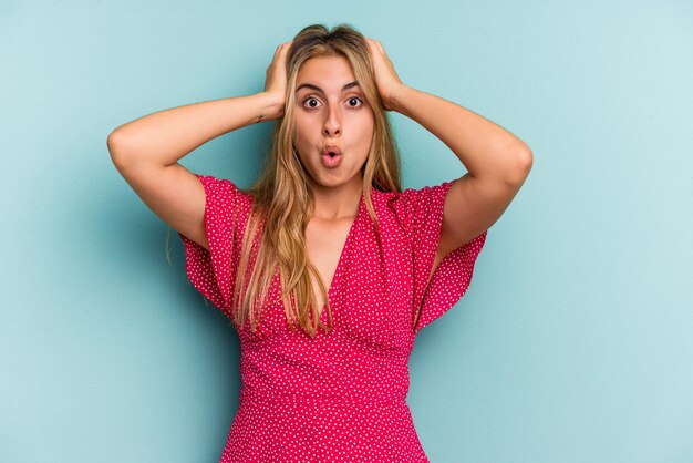 Young caucasian blonde woman isolated on blue background  surprised and shocked.