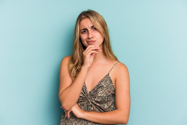 Young caucasian blonde woman isolated on blue background  thinking and looking up, being reflective, contemplating, having a fantasy.