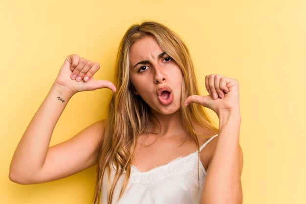 La giovane donna bionda caucasica isolata su sfondo giallo si sente orgogliosa e sicura di sé, esempio da seguire.