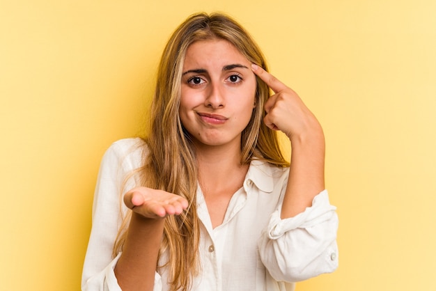 Young caucasian blonde woman isolated on yellow background  holding and showing a product on hand.