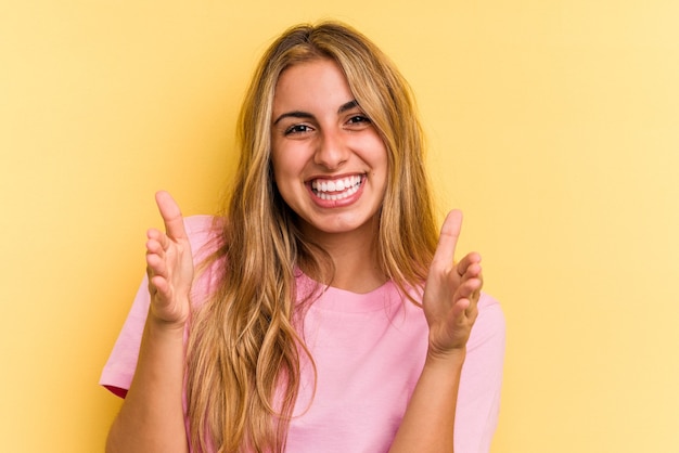 Young caucasian blonde woman isolated on yellow background  holding something with both hands, product presentation.