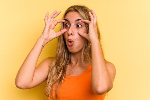 Young caucasian blonde woman isolated on yellow background  keeping eyes opened to find a success opportunity.