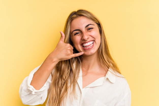 Young caucasian blonde woman isolated on yellow background  showing a mobile phone call gesture with fingers.