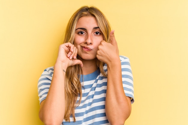 Young caucasian blonde woman isolated on yellow background  showing thumbs up and thumbs down, difficult choose concept