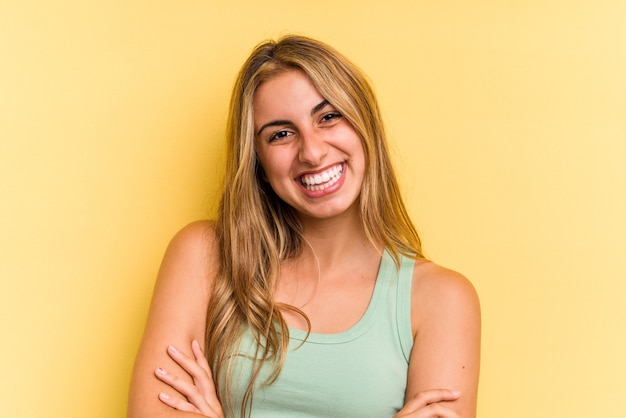 Young caucasian blonde woman isolated on yellow background  who feels confident, crossing arms with determination.