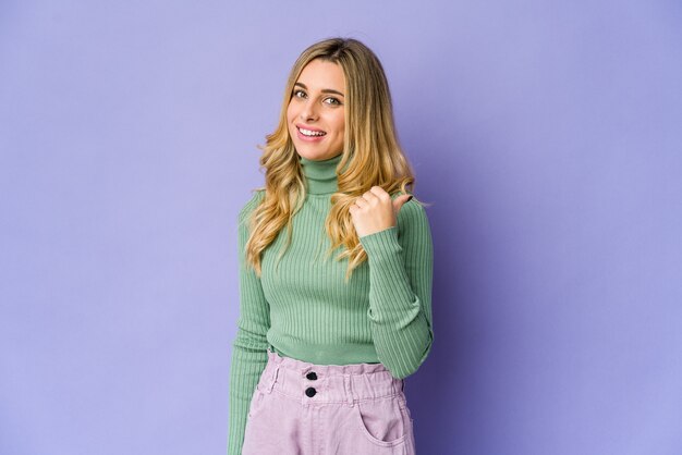 Young caucasian blonde woman points with thumb finger away, laughing and carefree.