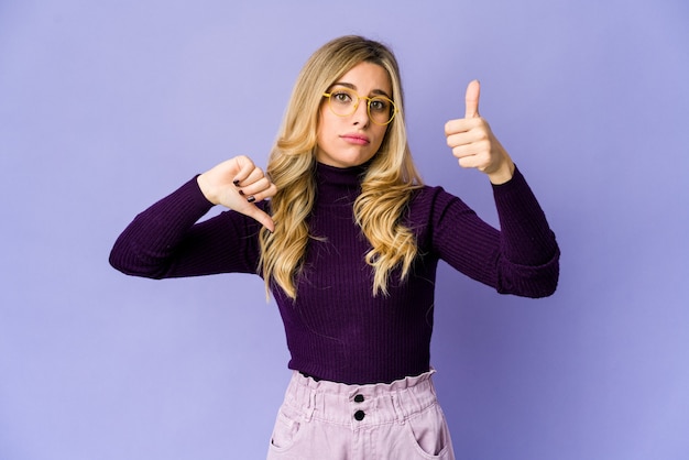 Young caucasian blonde woman showing thumbs up and thumbs down, difficult choose concept