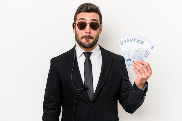 Young caucasian bodyguard man holding banknotes isolated on white background confused feels doubtful and unsure