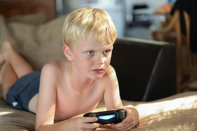 Young Caucasian boy playing video games at home on the sofa in soft afternoon light